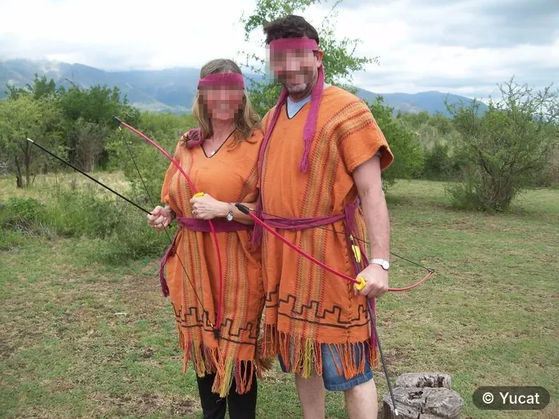 Una pareja con ponchos comechingones sostiene arcos, con las sierras de fondo.