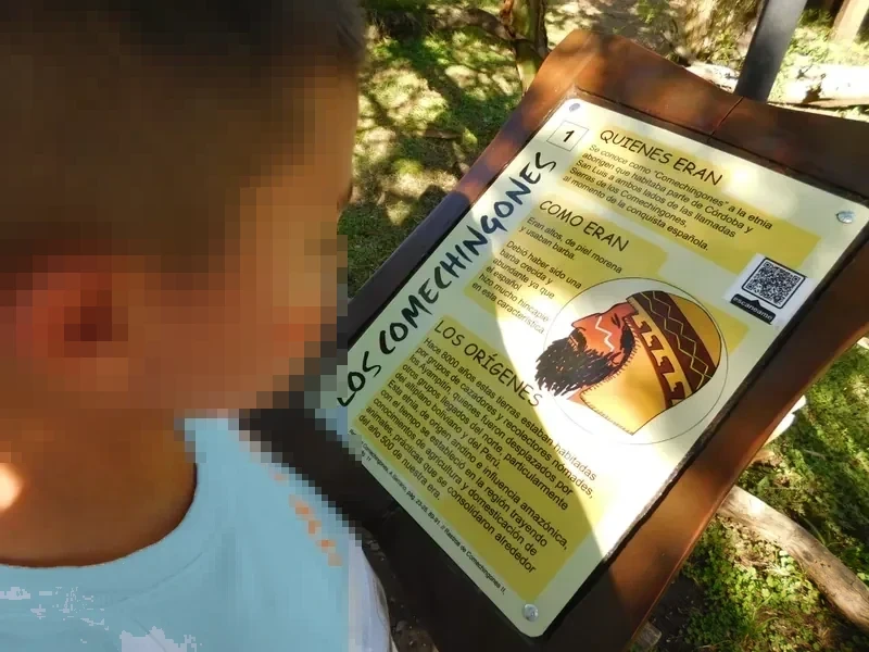 Un chico lee un cartel informativo numerado sobre los comechingones, con código QR.