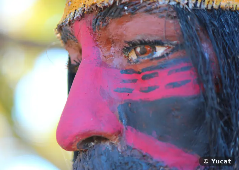 Detalle del rostro de una escultura con pintura de guerra roja y negra, de perfil.