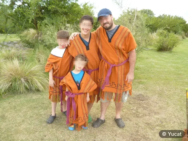 Una familia de cuatro personas vestida con ponchos comechingones, posando en el parque.