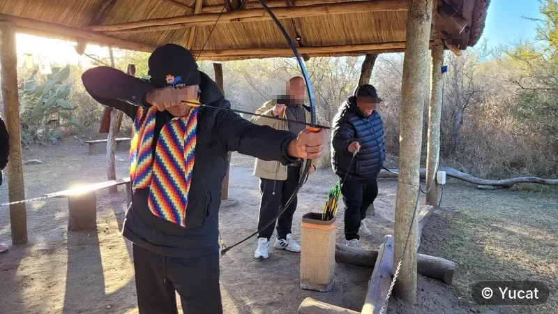 Un grupo de hombres adultos practicando tiro con arco bajo un quincho de paja.