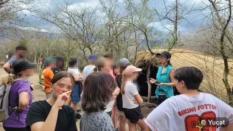 Una guía le explica a un grupo de visitantes junto al techo de paja de una casa-pozo.