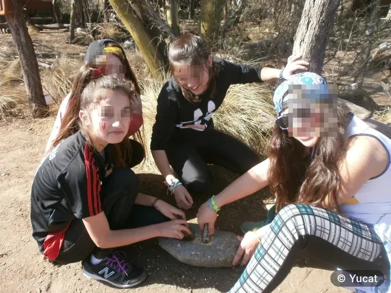 Un grupo de adolescentes con la cara pintada, alrededor de un mortero de piedra.
