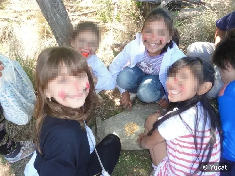 Un grupo de chicas con la cara pintada, en ronda alrededor de un mortero de piedra con granos.