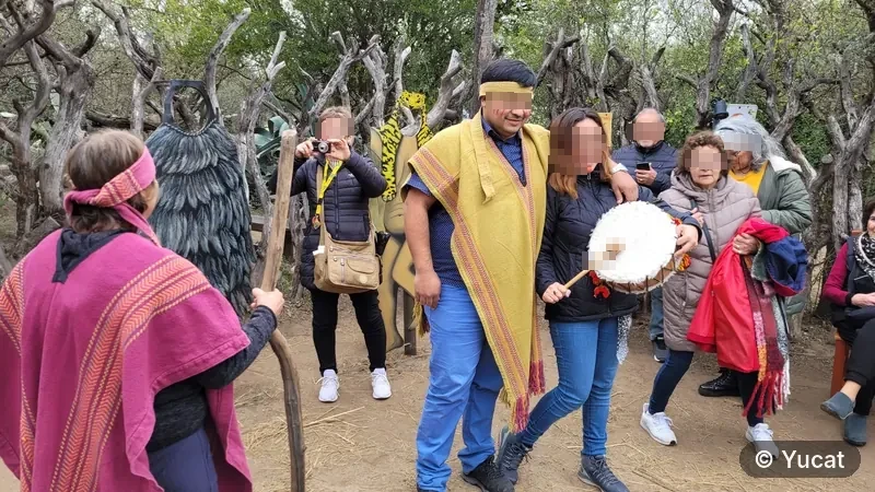 Un grupo de visitantes adultos con ponchos y la cara pintada, tocando un tambor ritual.