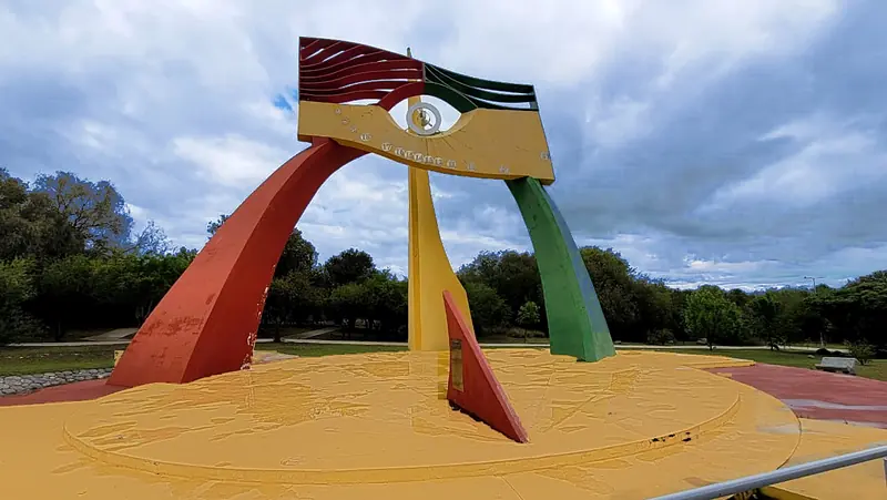 Foto: Yucat Parque Temático El reloj de sol «El Ojo del Tiempo»: arcos rojo, amarillo y verde que sostienen un cuadrante con forma de ojo, sobre una plataforma circular amarilla.