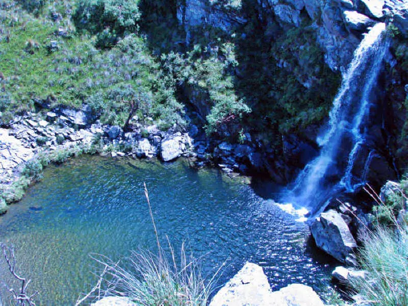 El Salto del Tigre: una cascada que cae entre rocas sobre una olla de agua azul, rodeada de vegetación serrana.