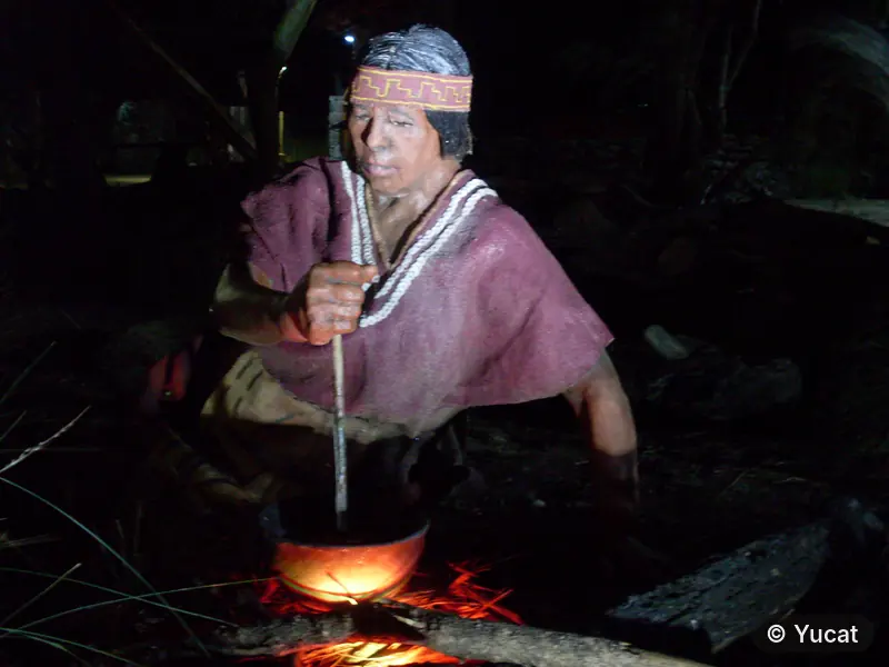 Escultura cocinando junto al fuego, revolviendo una olla de barro con un palo.