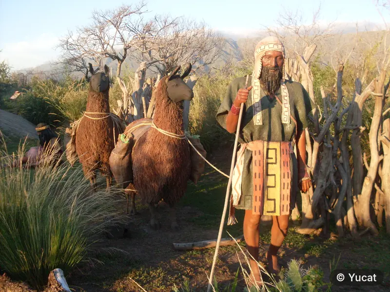Escultura con vincha y bastón, junto a dos llamas de carga.
