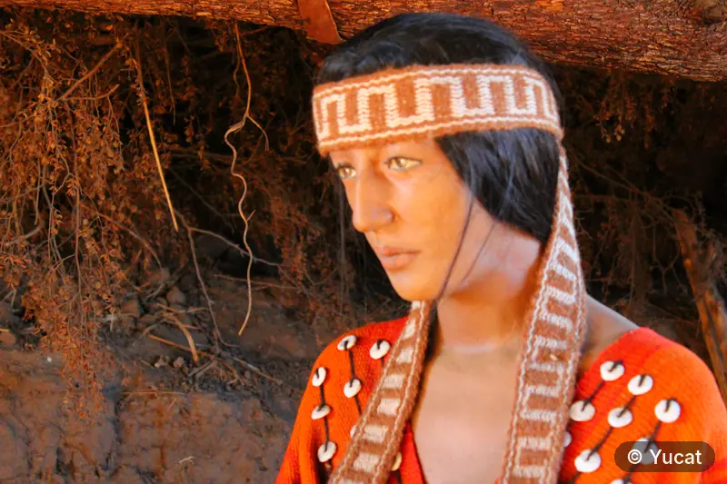 Escultura de un rostro comechingón con vincha tejida, junto al muro de tierra de una casa-pozo.