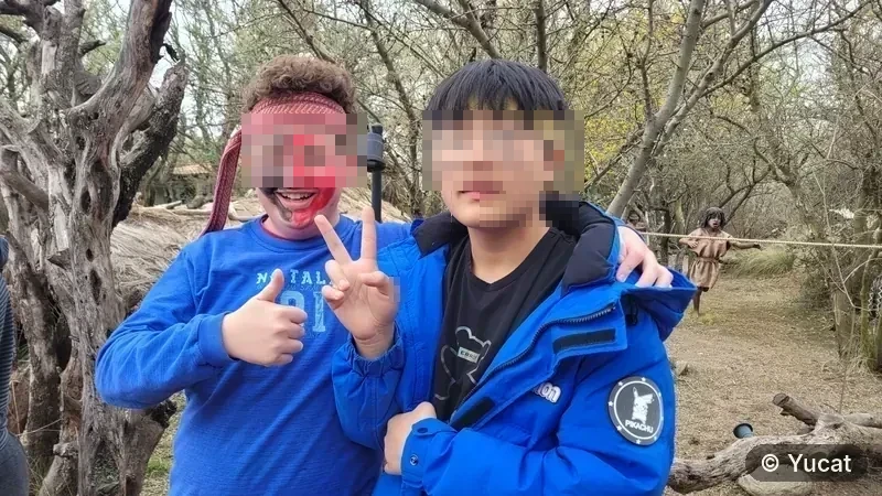 Dos adolescentes con pintura facial posando abrazados, con un sendero del parque de fondo.