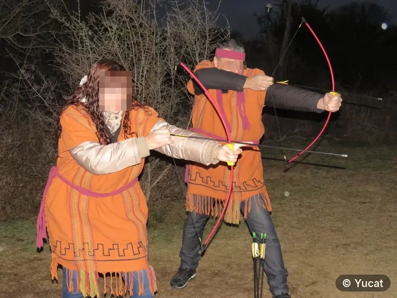 Dos adultos con vestimenta comechingona practican tiro con arco al aire libre.